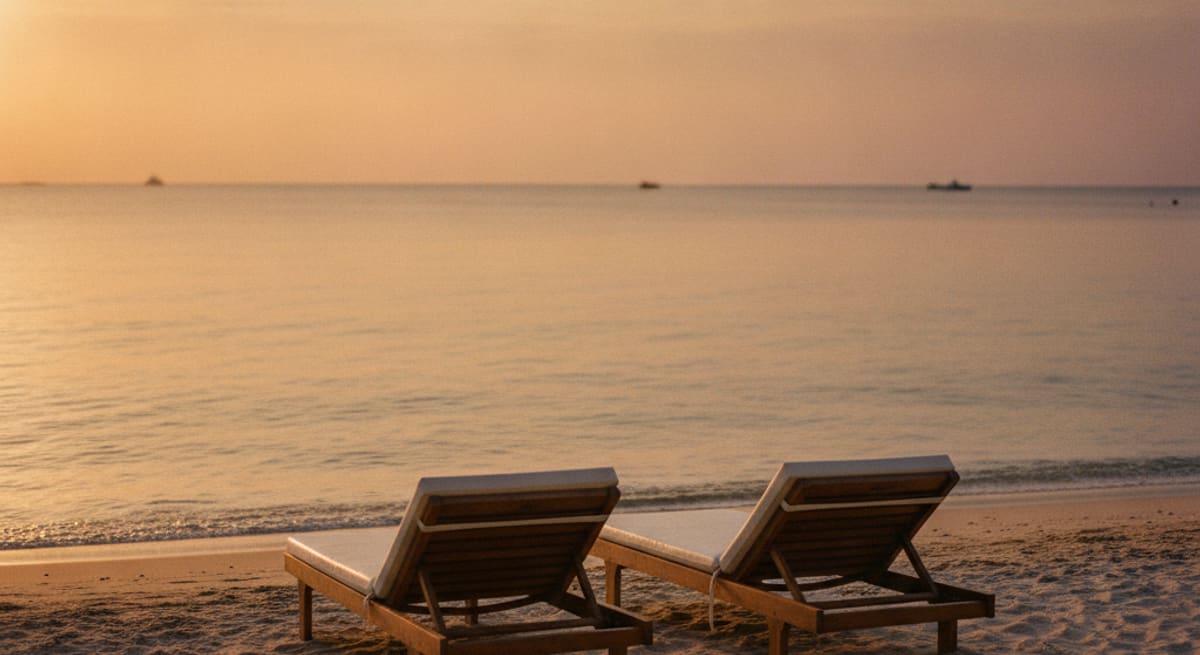 Zwei Liegestühle am menschenleeren Sandstrand bei Sonnenuntergang, warmes Licht, Blick aufs Meer